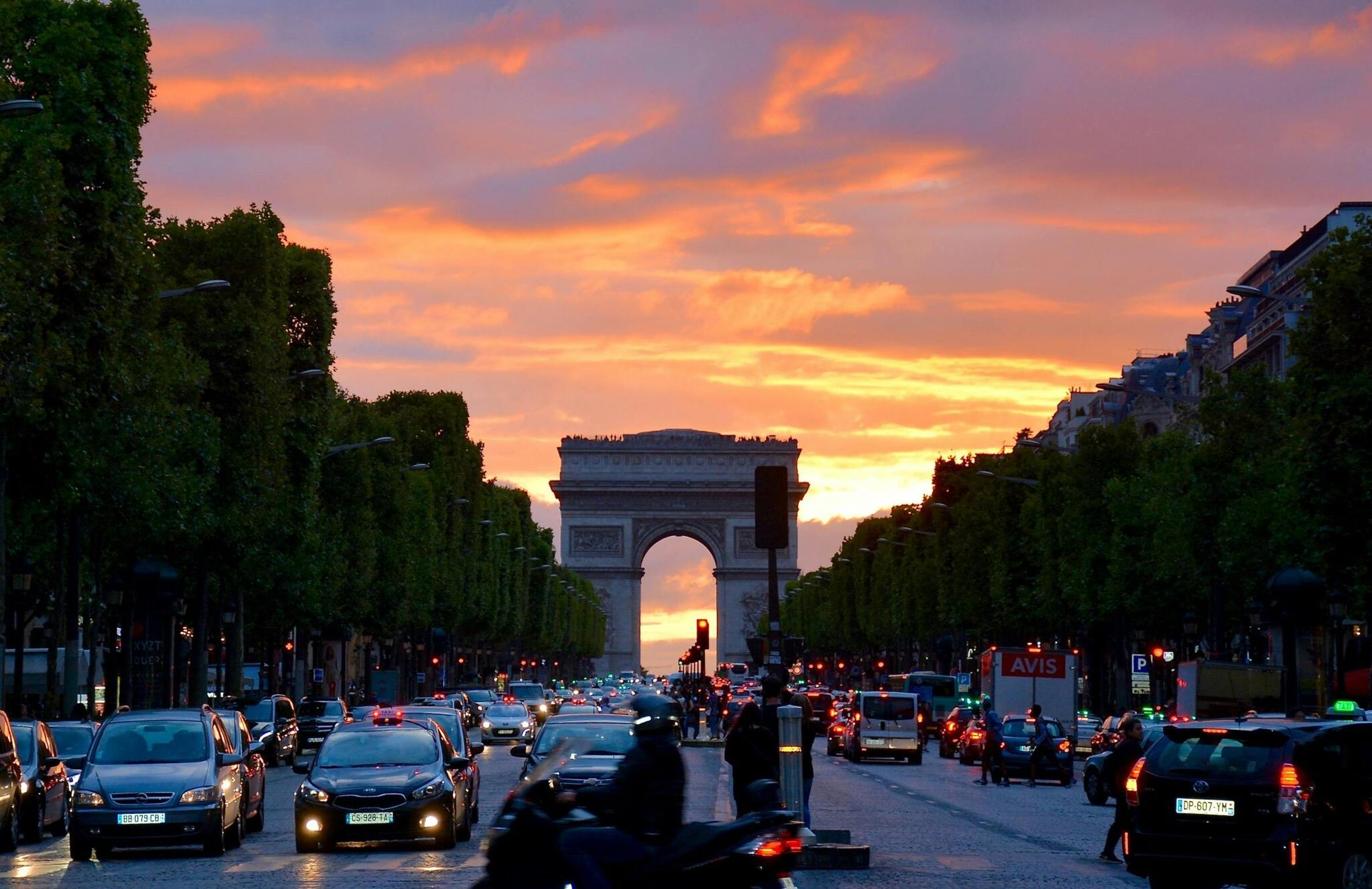 The Arc de Triomphe under a vivid sunset sky, with traffic circling the monument