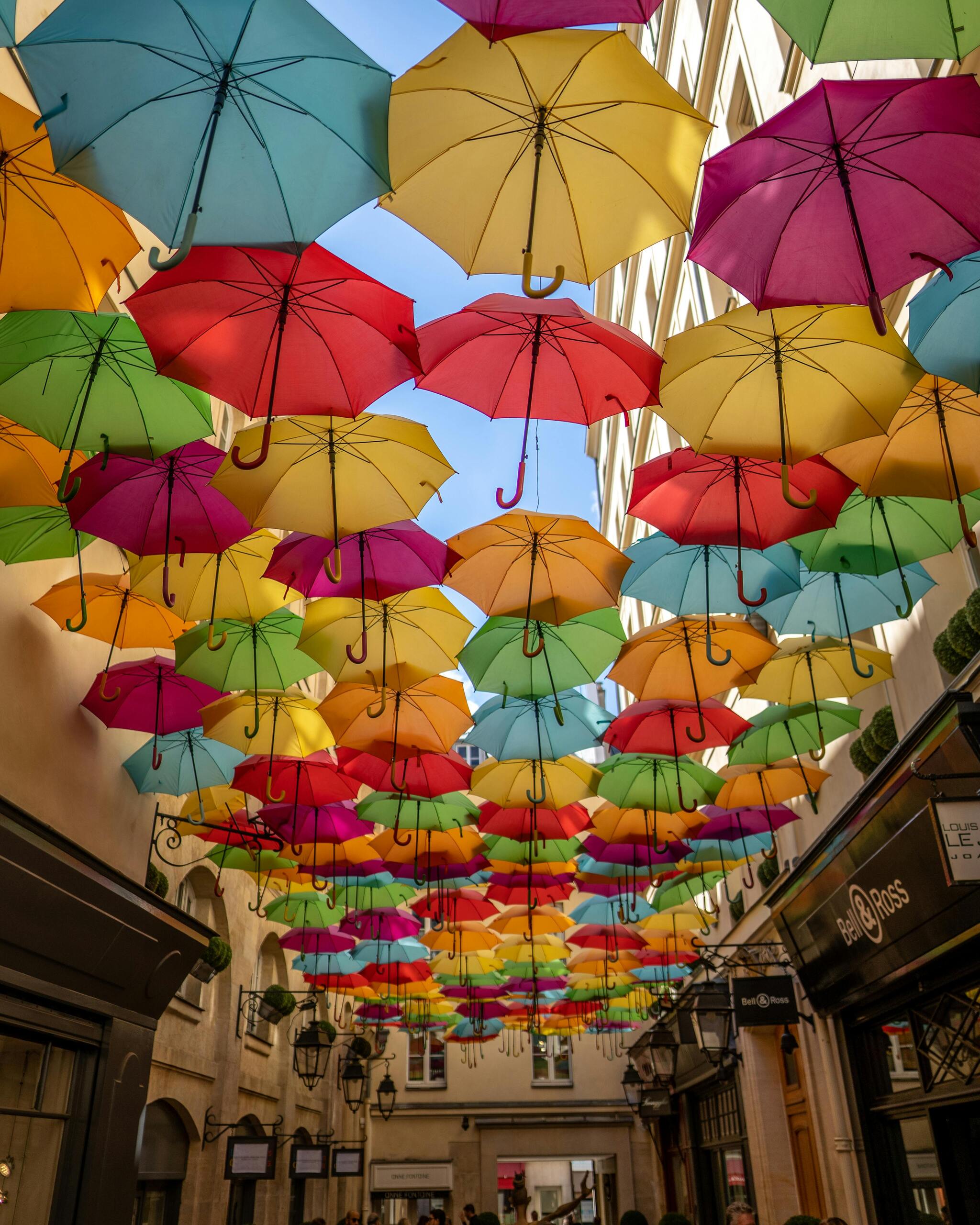 Colourful umbrellas suspended above a narrow Parisian street, forming a canopy