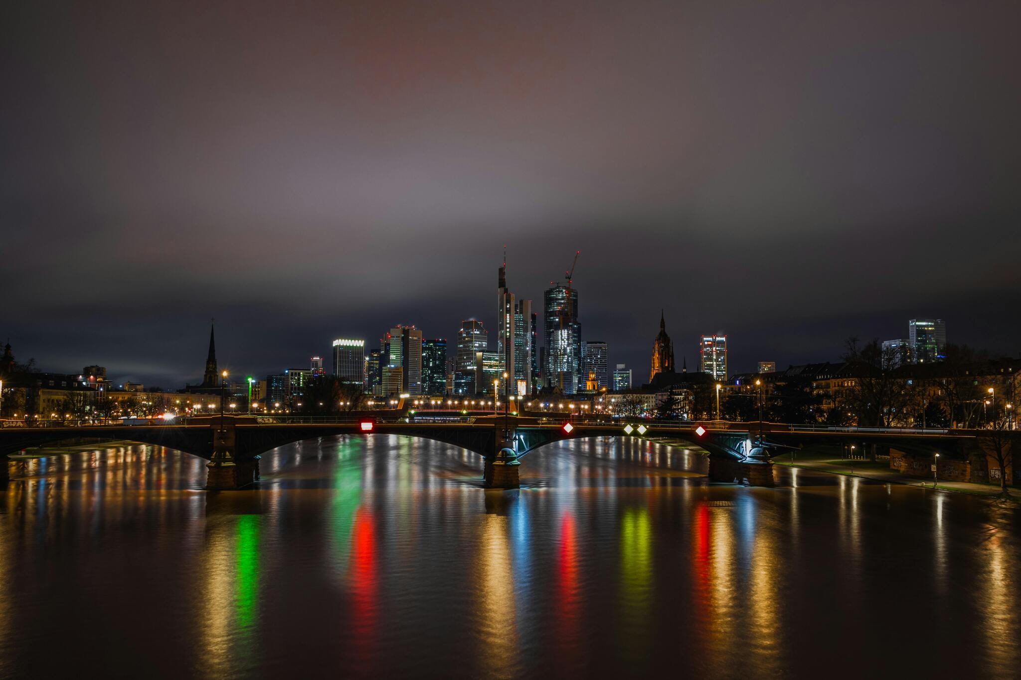 The illuminated Frankfurt skyline at night, with the Ignatz Bubis bridge reflected in the River Main